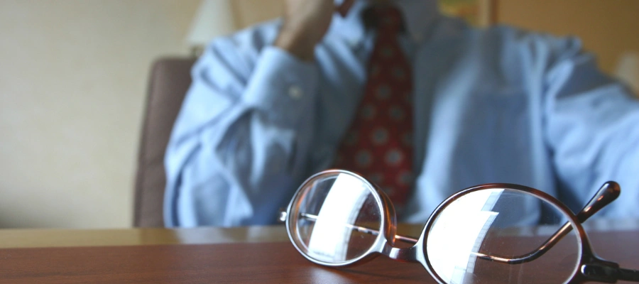 close up of eyeglasses on desk with middle section of businessman blurred in the background
