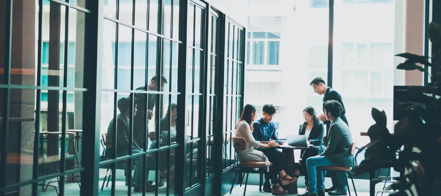 group of people talking at a table with a wall of windows