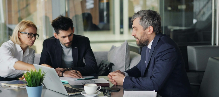 business professionals talk at table over papers and laptop