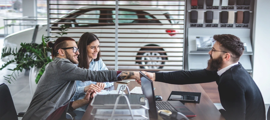 Woman and man in F&I office shaking hands with F&I manager over desk